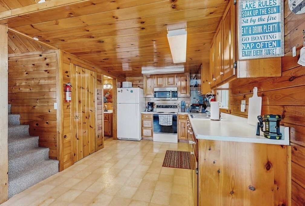 A cabin interior with a kitchen, wooden walls, a white refrigerator, and a fire extinguisher.