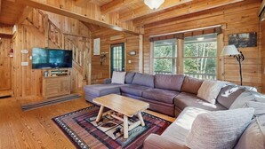 A wooden cabin interior with a large television, a sofa, a coffee table, and a fireplace. - Dog-friendly Lakefront Home With Deck, Grill, Wifi, Shared Dock & Water Access (Greenville)