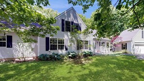 A two-story house with a well-maintained lawn and a small garden area. - Peaceful Home With Forest Views & Great Yard - Minutes to Town (Wiscasset)