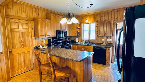 A kitchen with wooden cabinets, a granite countertop, a black refrigerator, and a chandelier. - Lake & Trail Landing- ATV & Snowmobile Access (Greenville)