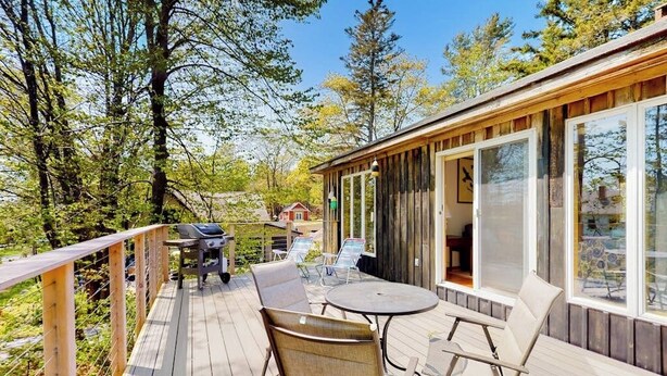 A wooden deck with outdoor furniture, a grill, and a view of the surrounding forest. - Cobb Nob (Southwest Harbor)
