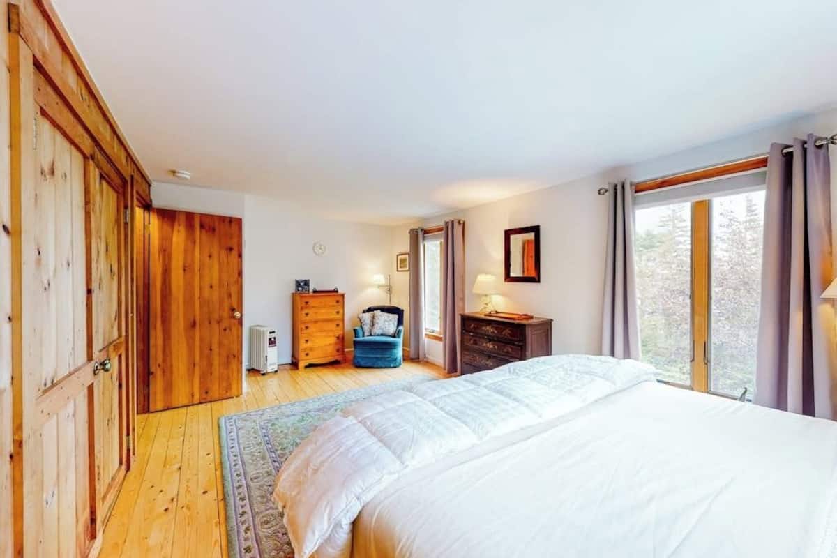 A bedroom with a large bed, wooden wardrobe, dresser, and a window with curtains.