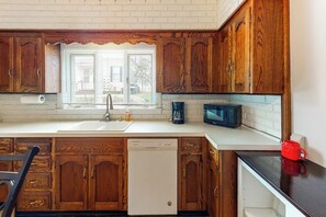 A kitchen with wooden cabinets, a dishwasher, a microwave, and a window with blinds. - Corbel House (Bucksport)