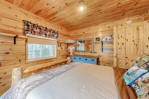 A wooden cabin bedroom with a bed, dresser, mirror, and window. - Lake-view Two-story Home With Beach Access, Wood Stove, Grill, W/d, & Fast Wifi (Greenville Junction)