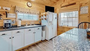 A cabin-style kitchen with wooden walls, a granite countertop, a refrigerator, and a clock on the wall. - Lake-view Two-story Home With Beach Access, Wood Stove, Grill, W/d, & Fast Wifi (Greenville Junction)