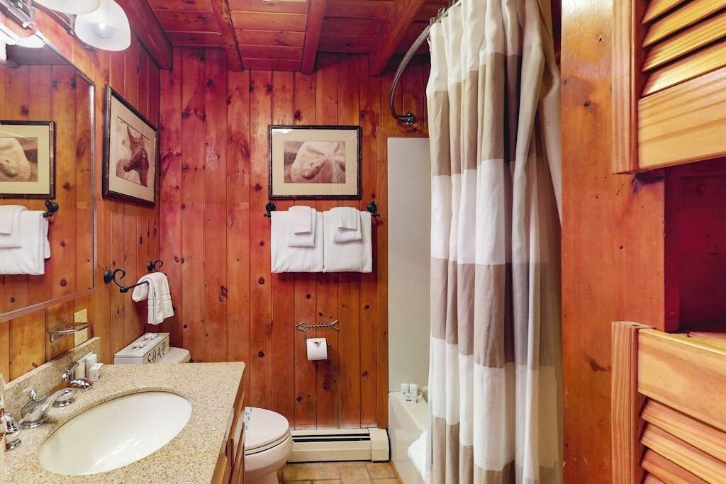 Een houten badkamer met een wastafel, toilet en douchegordijn.