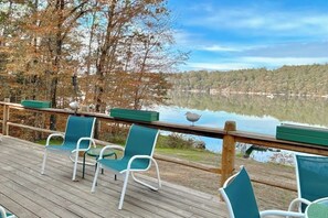 Eine Holzterrasse mit Stühlen und Geländer mit Blick auf einen See.