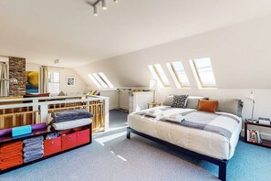 Ein geräumiges Schlafzimmer im Loft-Stil mit einem großen Bett, Dachfenstern, einem Schreibtisch und Stauraumelementen.