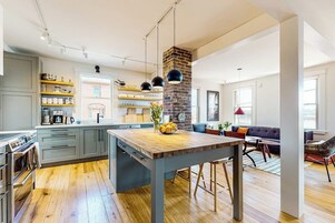A modern kitchen with a central island, wooden flooring, and a brick accent wall.