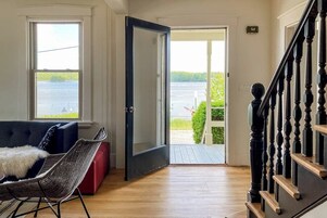 A room with a view of a body of water, a door leading outside, a staircase, and a sofa with a furry throw.