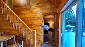 Ein Interieur einer Holzhütte mit Treppe, Essbereich und Blick auf eine verschneite Landschaft.