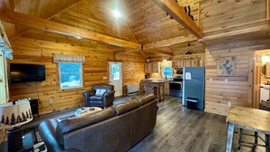Ein Holzhütten-Interieur mit Wohnzimmer, Sofa, Fernseher, Küchenbereich und Holzwänden.