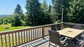 A wooden deck with a table and chairs, surrounded by a wooden railing, overlooking a forested area. - Moosehead State of Mind, 3BR Cabin With Mtn Views & Deck (Shirley)