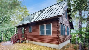A log cabin with a metal roof, a wooden deck, and a small porch. - Lakefront Home With Private Dock, Canoe & Kayak, Fast Wifi, and Firepit - dog OK (Greenville)