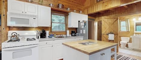 A kitchen with white cabinets, a stove, a microwave, and a refrigerator.