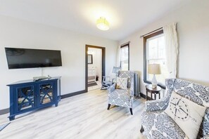 Ein Wohnzimmer mit Fernseher, blauem Schrank, gemustertem Sofa und einem Sessel.
