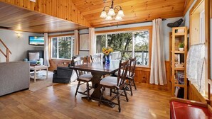 A wooden interior with a dining table, chairs, a sofa, and a TV. - Settlers Cottage, Cute Maine Home With Water Views (Cushing)