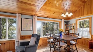 A wooden interior with a dining table, chairs, a sofa, and large windows. - Settlers Cottage, Cute Maine Home With Water Views (Cushing)