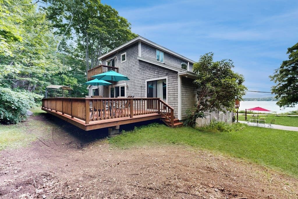 A two-story house with a deck, a covered patio, and a view of a lake.