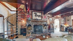 Ein geräumiges Wohnzimmer mit Kamin aus Backstein, einer Holztreppe und Ledermöbeln.