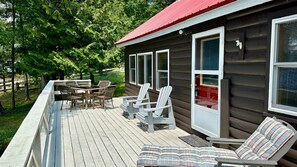 A wooden deck with outdoor furniture, including chairs and a table, and a cabin with a red roof. - Dog-friendly Lakefront Cabin With Full Kitchen, Firepit, Free Wifi, Great Views (Greenville)