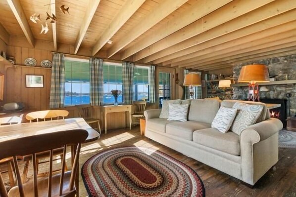 Interior acogedor de una cabaña con techo de madera, un sofá, una mesa de comedor y una chimenea.
