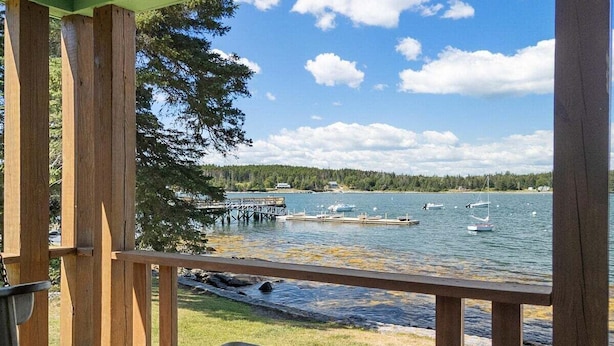 A wooden deck with a view of a lake, dock, and boats. - Marshall Point Cottage, Classic 5-bedroom (Tenants Harbor)