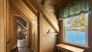 A wooden interior with a window overlooking water, a bench, and a door leading to another room. - Marshall Point Cottage, Classic 5-bedroom (Tenants Harbor)