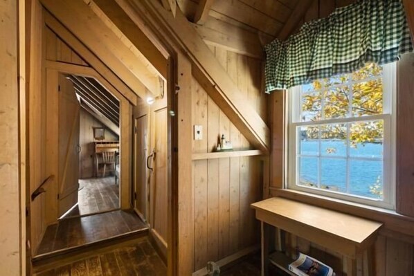 A wooden interior with a window overlooking water, a bench, and a door leading to another room. - Marshall Point Cottage, Classic 5-bedroom (Tenants Harbor)