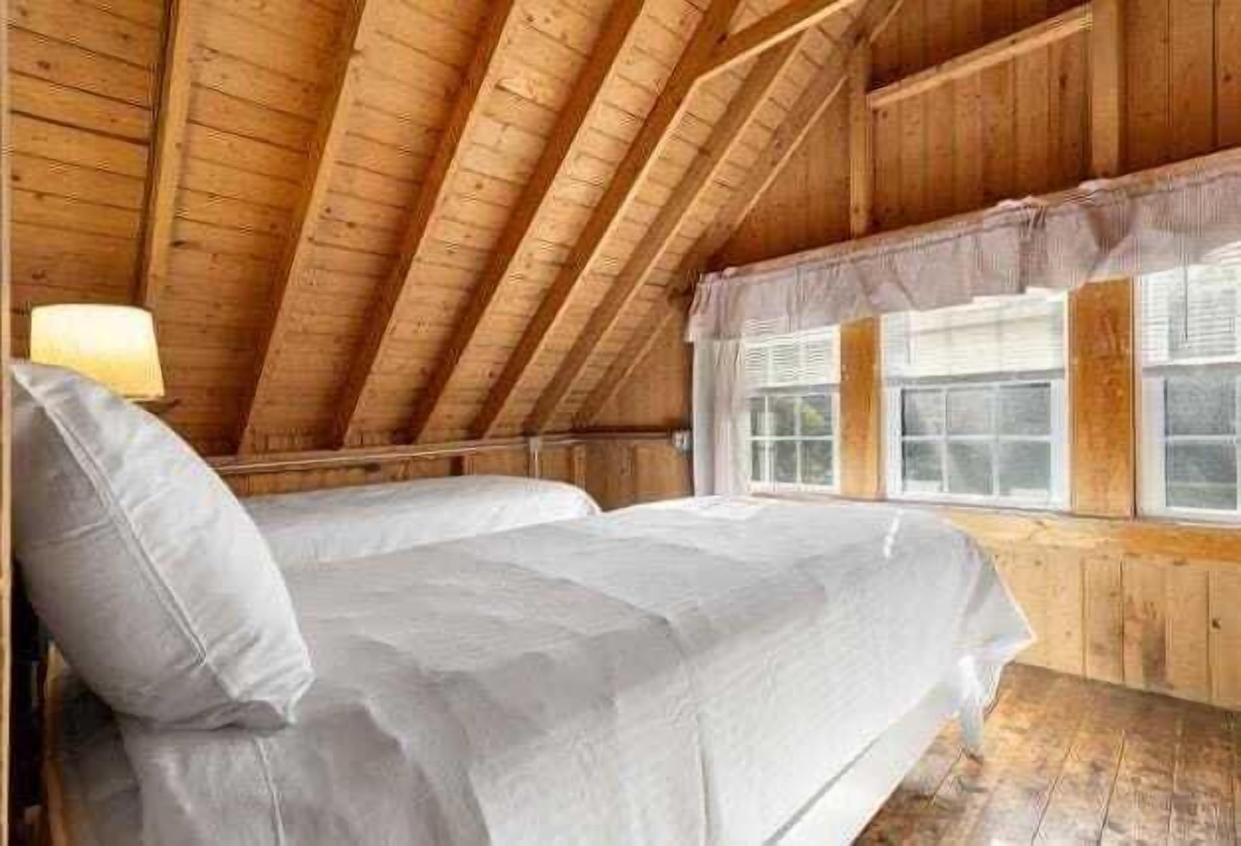 Un dormitorio de ático con suelo de madera, una cama individual apilada, una ventana con cortinas y una lámpara a la izquierda.