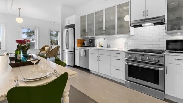 A modern kitchen with white cabinets, a stainless steel oven, and a dining area with a table set for two. - Rockland Central (Rockland)