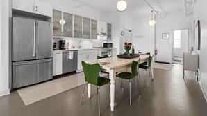 A modern kitchen with stainless steel appliances, a dining area with a wooden table and green chairs, and a visible clock on the wall. - Rockland Central (Rockland)