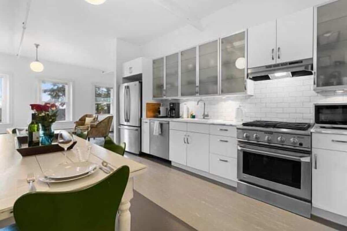 Una cocina moderna con armarios blancos, una estufa de acero inoxidable y un comedor con una mesa lista para dos.