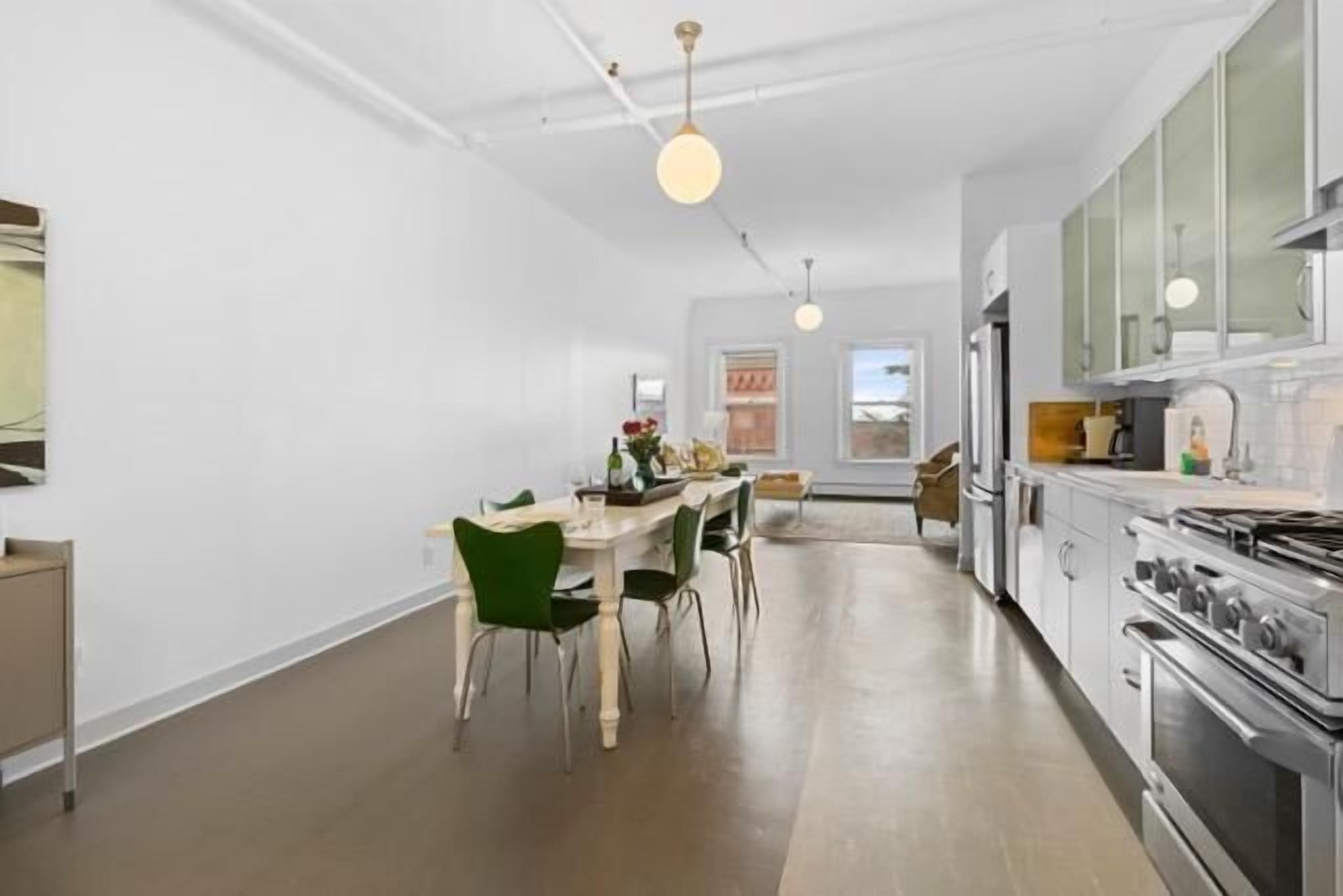 A modern kitchen with a dining area, white walls, and a large window.
