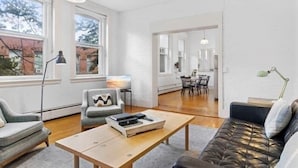 A modern living room with a sofa, armchair, coffee table, and a dining area in the background. - Rockland Central (Rockland)