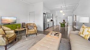 A modern living room with a sofa, armchair, and coffee table, a TV, and a kitchen in the background. - Rockland Central (Rockland)
