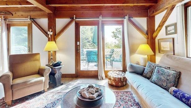 A cozy room with a wooden ceiling, a sofa, a chair, a small table, and a window with curtains. - Romley House Deck & New Luxe Kitchen Near Boothbay Harbor (Southport)