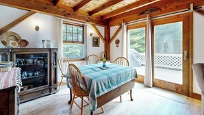 A wooden interior with a dining table, chairs, a fireplace, and large windows. - Romley House Deck & New Luxe Kitchen Near Boothbay Harbor (Southport)