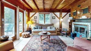 A cozy room with a wooden ceiling, a sofa, a fireplace, and a large window. - Romley House Deck & New Luxe Kitchen Near Boothbay Harbor (Southport)