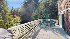 A wooden deck with a white lattice railing, green chairs, and a green umbrella. - Romley House Deck & New Luxe Kitchen Near Boothbay Harbor (Southport)