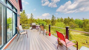Een terras met stoelen, een barbecue en uitzicht op bomen.