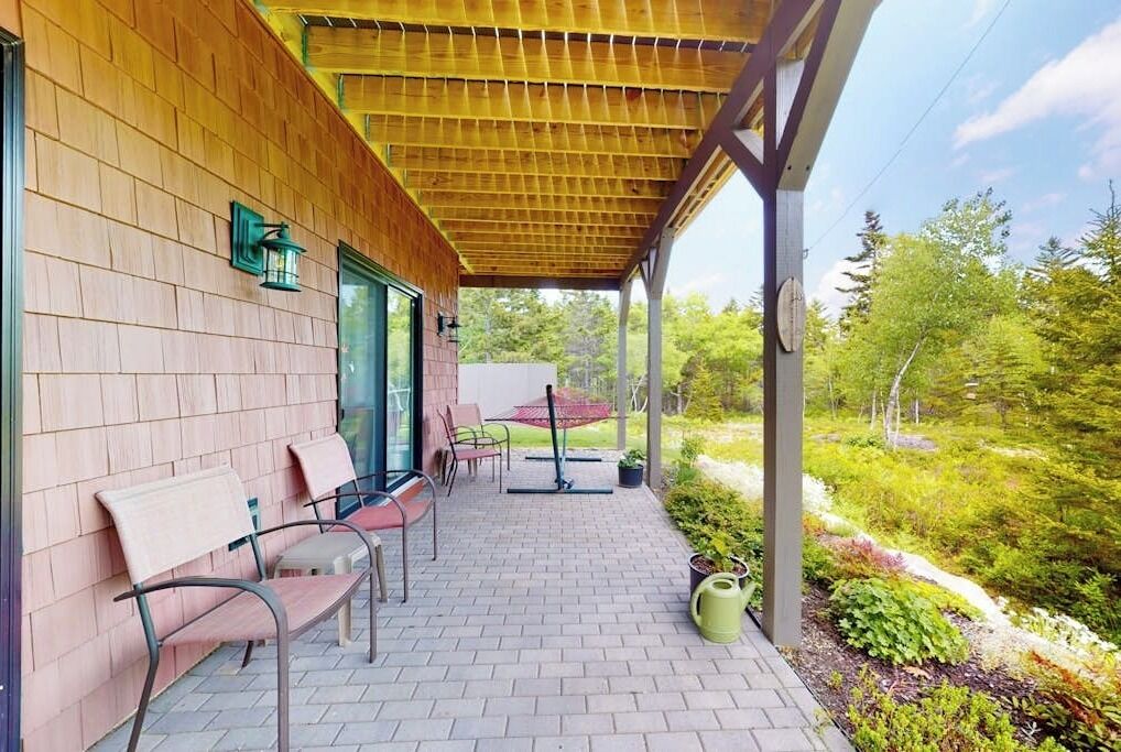 A covered outdoor seating area with chairs and a table, surrounded by a wooden wall and a garden.