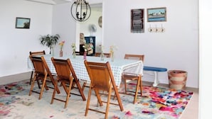 Een eetruimte met een tafel voor vier personen, omringd door houten stoelen, een kleurrijk tapijt en een hanglamp.
