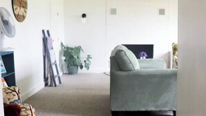 Een woonkamer met een bank, een ventilator, een klok en een plant.