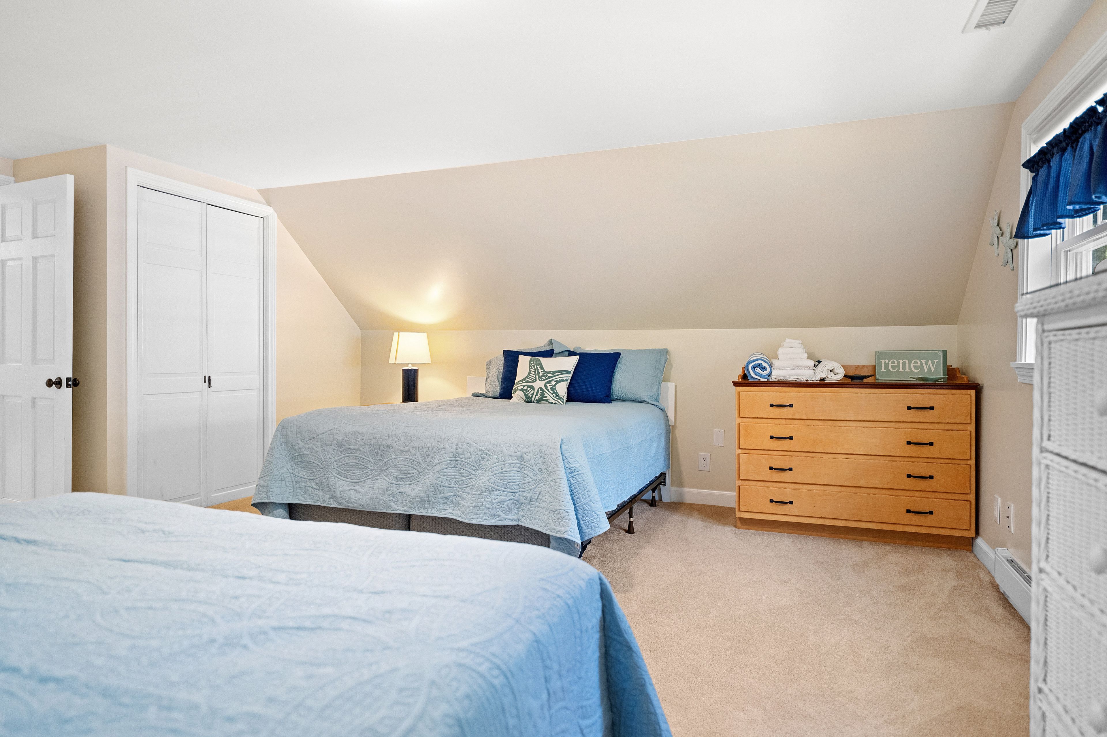 A bedroom with two beds, a dresser, and a lamp.