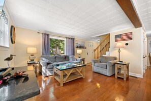 A spacious living room with a wooden floor, a sofa, a coffee table, and a lamp. - Boothbay Harbor Home With Water Views Near Dining & Whale Watching (East Boothbay)