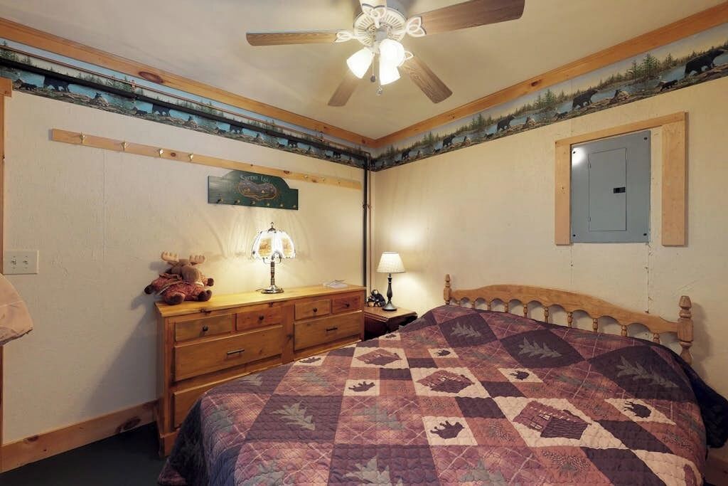 Un dormitorio con cabecera de madera, colcha acolchada, cómoda con lámpara y ventilador de techo.