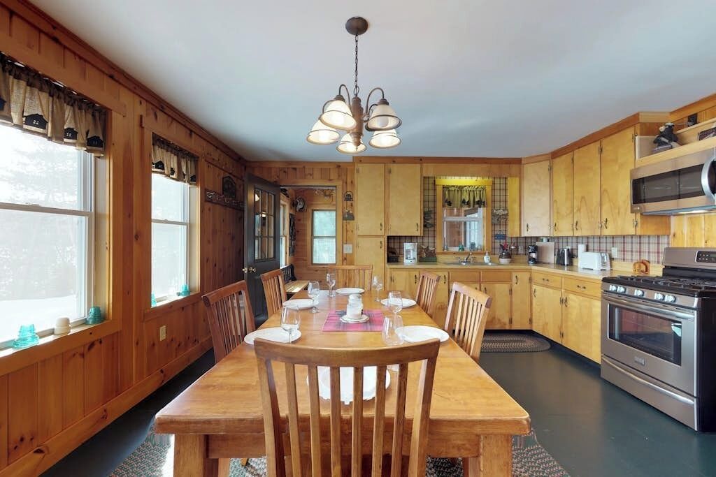 A wooden interior with a dining table set for four, a kitchen with wooden cabinets, and a stainless steel oven.