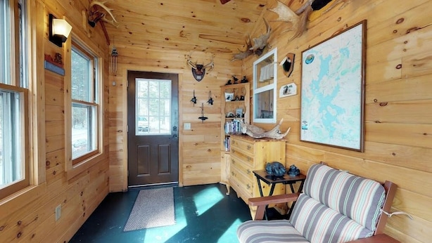 Interior de uma cabana de madeira com um sofá, um mapa e chifres nas paredes.