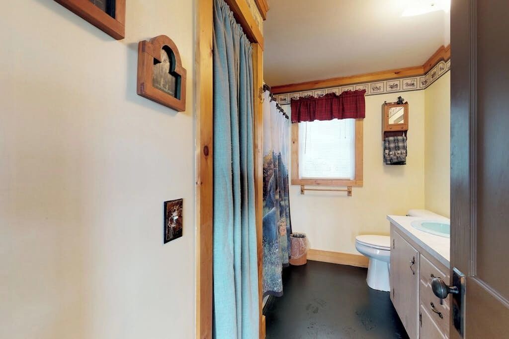 A narrow hallway leading to a bathroom with a toilet, sink, and a mirror.